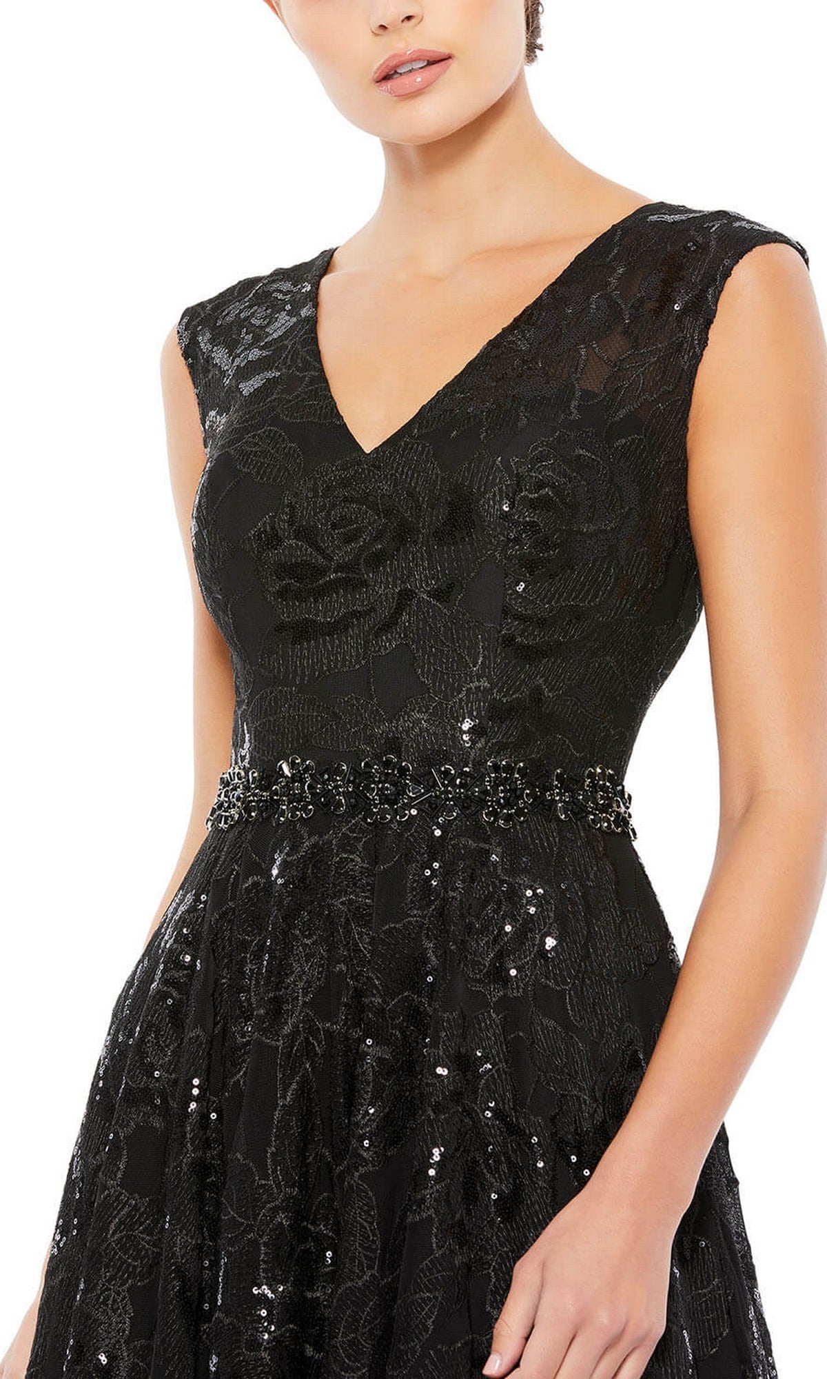 A woman wearing the Long Formal Dress 12413 by Mac Duggal, a sleeveless black gown with a V-neckline, subtle floral embroidery, and a beaded waistband, shown from shoulders to waist.